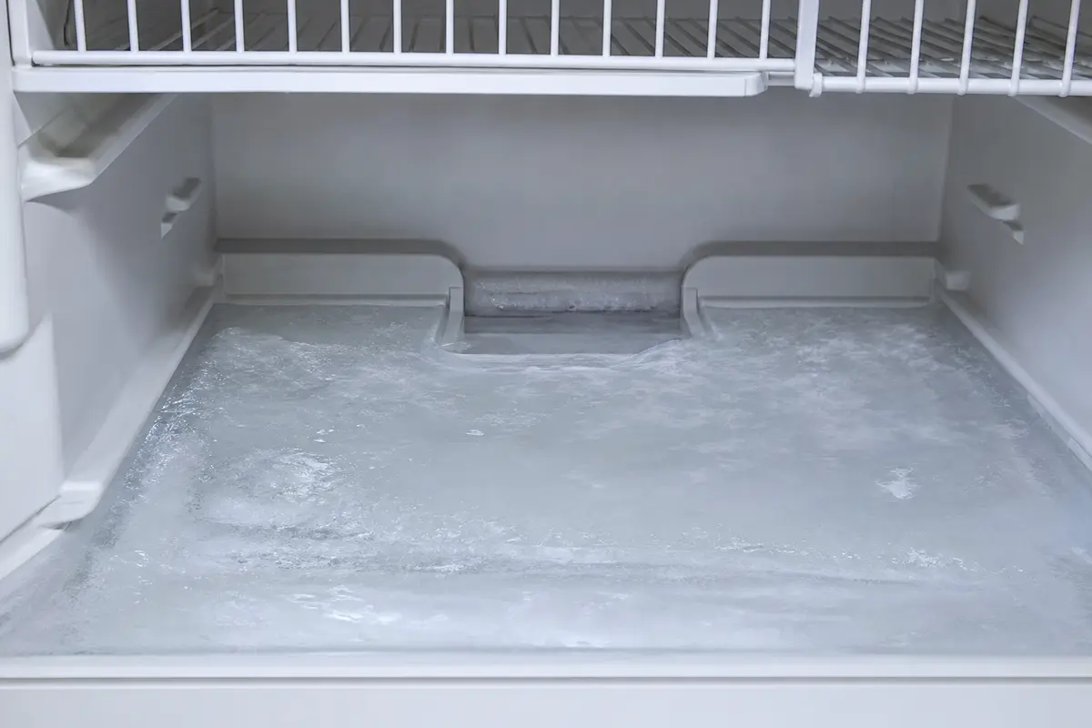 Smooth clear ice sheet across freezer floor below bottom basket near rear drain channel
