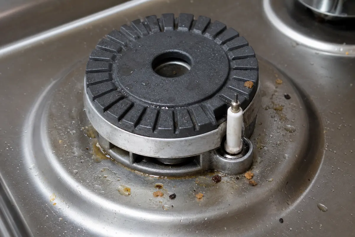 Cooktop burner igniter close-up with moisture and food debris near the spark point