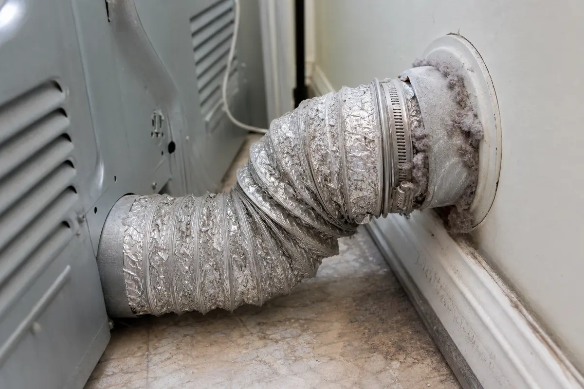 Dryer pulled forward with lint packed around a kinked vent hose and wall exhaust connection