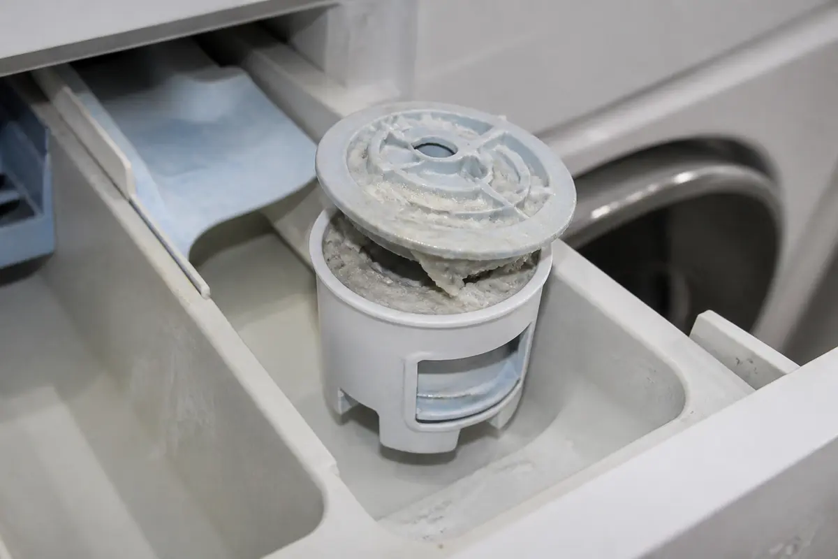 Fabric softener siphon cap with cloudy buildup blocking the dispenser opening
