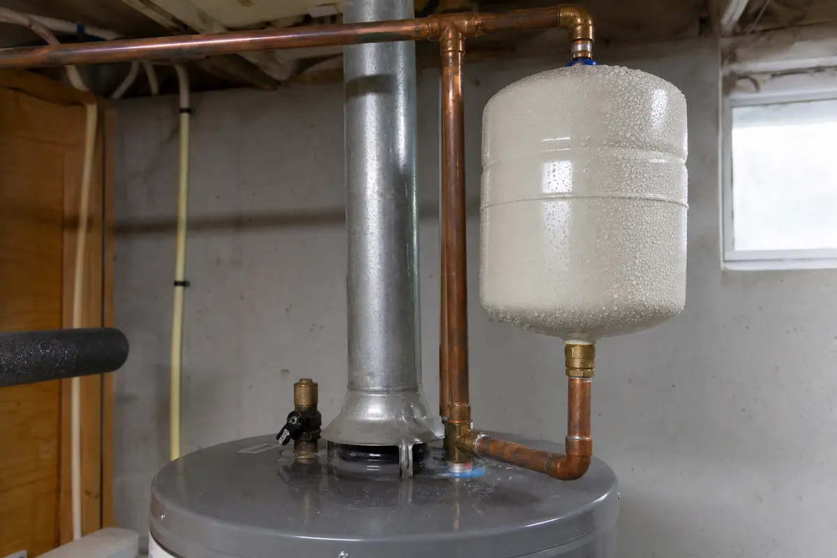 Water heater expansion tank with condensation beads across the shell above a tank water heater