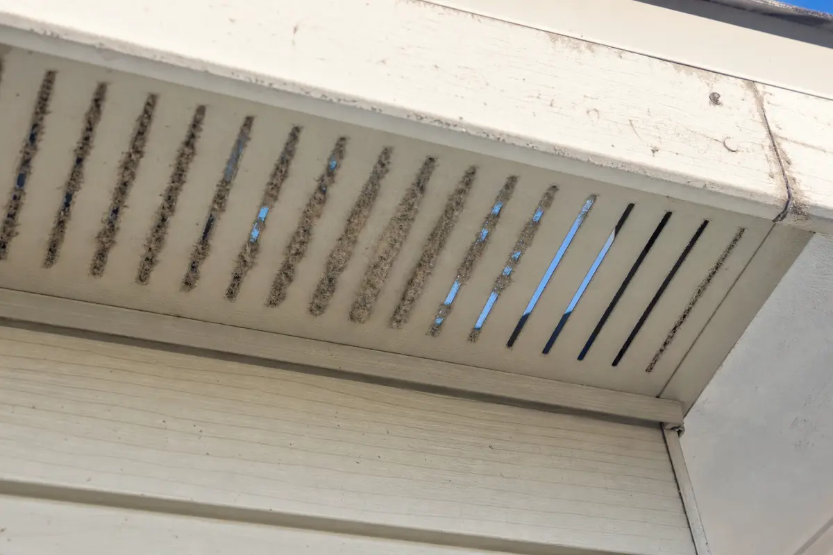 Exterior soffit vent cover with dust and debris clogging several intake slots