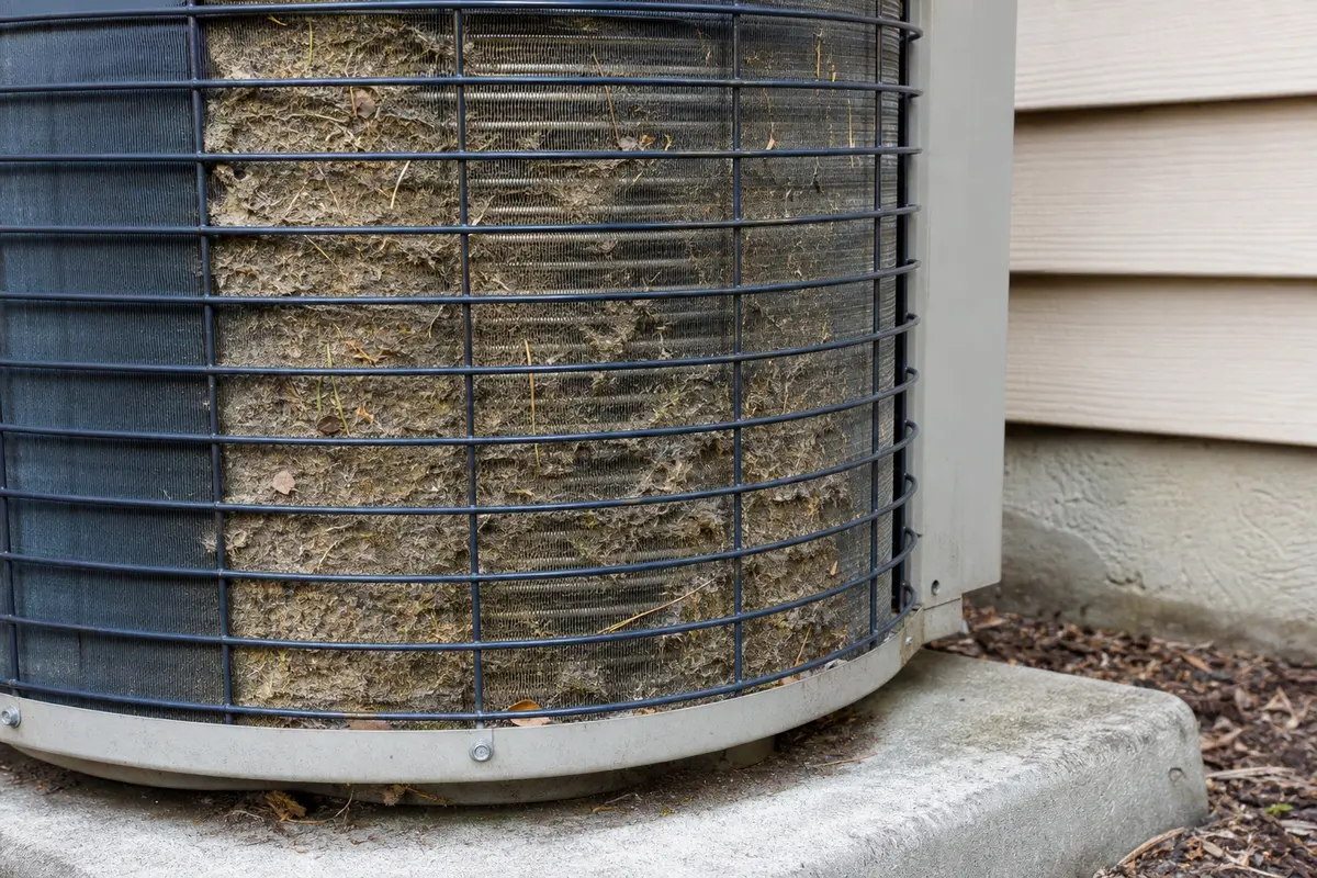 Dirty outdoor condenser fins packed with debris on an air conditioner that keeps running