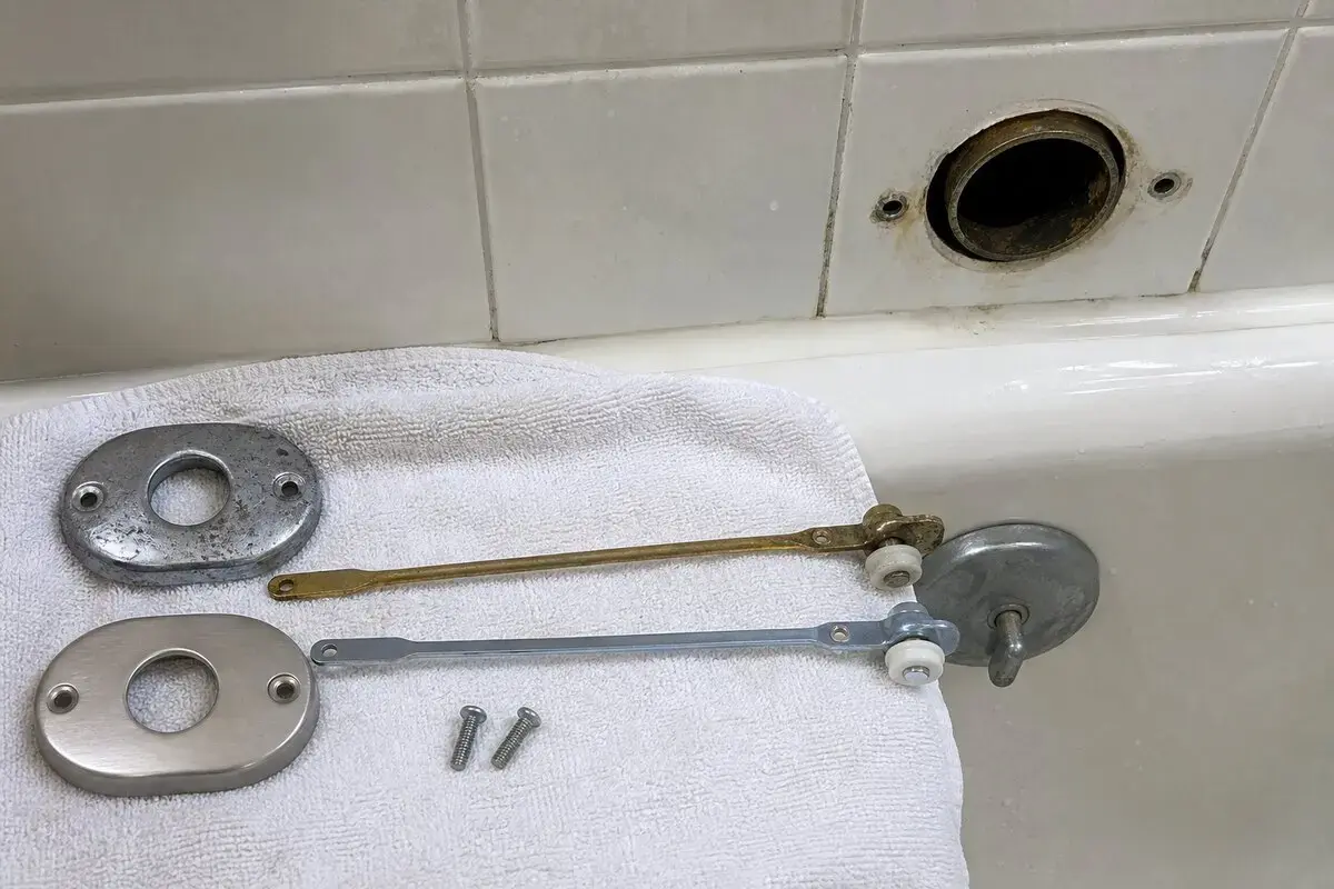Bathtub overflow plate removed with trip lever linkage exposed on a towel