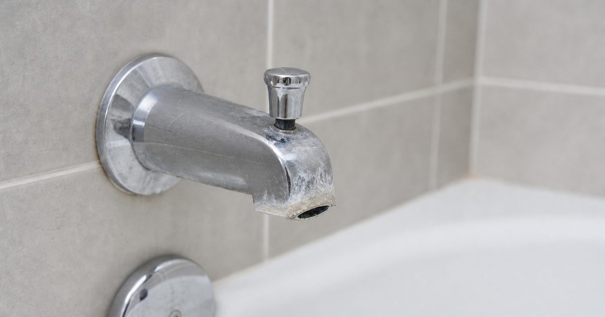 Chrome bathtub spout with mineral buildup around the outlet and diverter